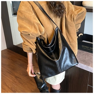 Sac seau hobo noir brillant porté avec un manteau marron pour un look citadin moderne