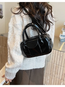 Close-up of black glossy leather bowling bag worn with a white knit sweater