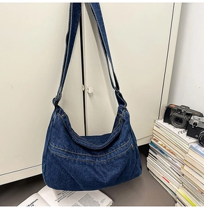 Detail of blue denim crescent crossbody bag with zipper pockets and adjustable strap