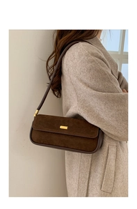Détail du sac baguette en daim marron foncé avec boucle dorée et bandoulière en cuir fin