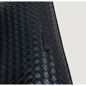 Close-up of black woven leather texture and embossed Pluto & Charon brand tag