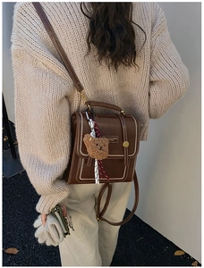 Détail du sac à dos vintage en cuir marron avec surpiqûres et breloque ours en peluche