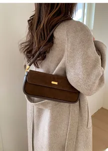 Vue détaillée du sac sous le bras en daim marron avec boucle dorée sur manteau beige
