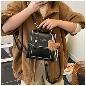 Détail d'un sac à dos rétro noir avec surpiqûres blanches et porte-clé ours