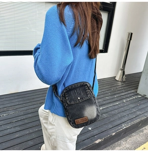 Detail of a black denim crossbody phone bag with vintage silver stud and leather patch