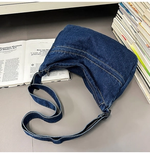 Macro detail of dark blue denim shoulder bag with contrast stitching on soft crescent shape