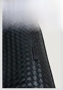 Detail shot of black woven leather texture and a sewn logo tag on the tote bag