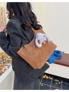 Close-up of caramel suede tote bag with cute white rabbit plush charm for autumn fashion