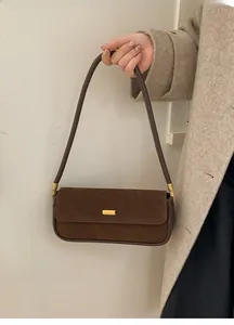 Vue détaillée du sac bandoulière en daim marron mat avec boucle dorée sur un manteau beige