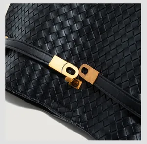 Detail of black woven leather texture and vintage gold buckle on a crossbody tote bag