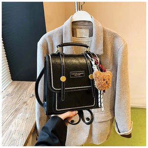 Détail du mini sac à dos en cuir noir avec coutures blanches et breloque ours