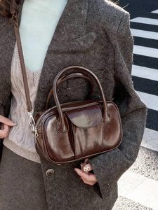 Deep brown glossy leather bowling bag with top handles and strap in urban street view