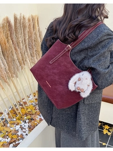 Macro shot of burgundy faux suede tote bag detail with plush bunny charm and strap
