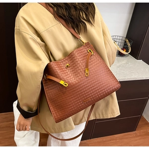 Detail of woven leather tote bag in caramel brown with gold hardware on a beige trench coat