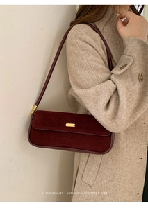Détail du sac baguette en daim bordeaux avec boucle dorée sur un manteau en laine beige