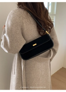 Détail du sac baguette noir en daim avec boucle dorée porté sur un manteau beige