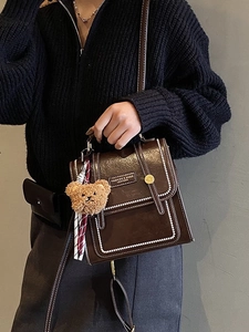Sac à dos rétro en cuir marron foncé avec surpiqûres blanches et ours sur un mannequin femme