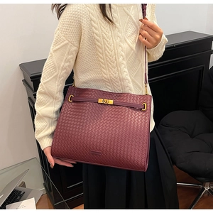 Detail of burgundy woven leather tote bag with gold buckle on a model in a white sweater