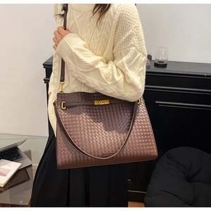 Detail of deep brown woven tote bag showing leather texture and gold buckle on shoulder strap