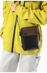 Detail of a minimalist crossbody phone bag with a brown flap and black snap buttons