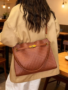 Large dark brown woven leather tote bag with gold buckle worn over the shoulder