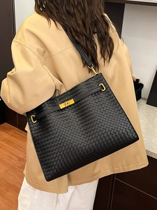 Large black woven leather tote bag with gold metallic clasp shown on a model