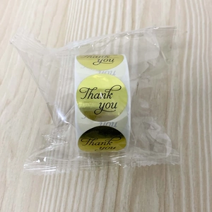 Close-up of gold glossy Thank You stickers roll in clear protective plastic wrap