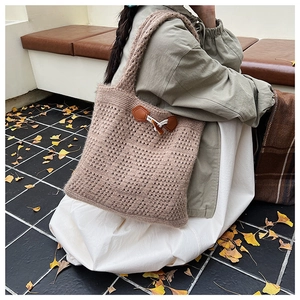 Detail of a beige cable-knit tote bag with retro toggle closure and leather base