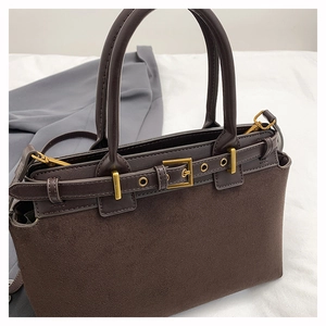 Detailed close-up of brown suede handbag with golden buckle and belt strap accents