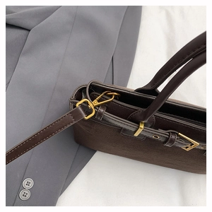 Detail of dark brown suede handbag featuring polished gold hardware and detachable shoulder strap