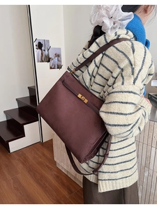 Détail du sac fourre-tout en daim marron foncé avec fermoir doré porté par un mannequin chic