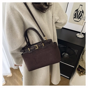 Detail of dark brown suede handbag with gold buckle, worn crossbody by a female model