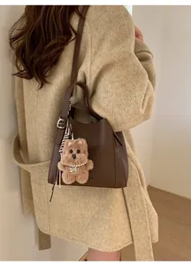 Detail of dark brown lychee leather bucket bag with cute bear charm and woven rope