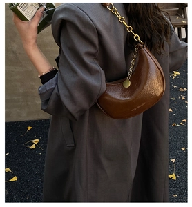 Detail of dark brown crescent bag with glossy crinkle texture and gold chain strap