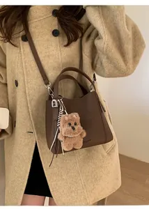 Detail of a dark brown pebble grain leather bucket bag with a cute plush bear charm