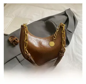 Detail of a brown leather crescent bag with glossy texture and gold chain strap