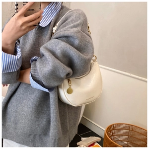 Detail of white crescent shoulder bag with embossed texture and gold round pendant