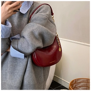 Detail of wine red patent leather dumpling bag with gold chain and branded charm