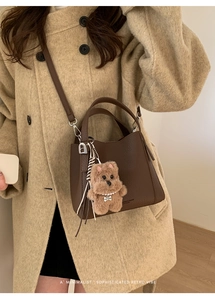 Detail of a brown lychee pattern leather bucket bag with a cute plush bear charm