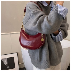 Close-up of a burgundy leather crescent bag with gold chain strap on a grey sweater