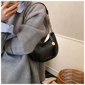 Close-up of black glossy dumpling bag with chunky gold chain and metallic pendant