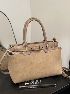 Brown suede patchwork handbag with metal buckle and shoulder strap on a book