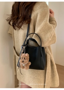 Close-up of black lychee leather bucket bag with a cute brown plush puppy charm pendant