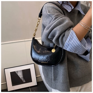 Detail of black wrinkled patent leather hobo bag with gold chain and metal charm
