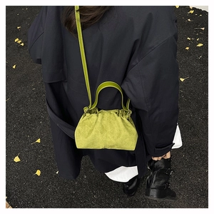 Close-up of green ruched cloud bag in suede-like texture on ginkgo leaf background