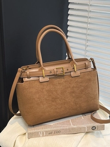 Brown faux suede handbag with leather trim and gold buckle, shown in a refined interior