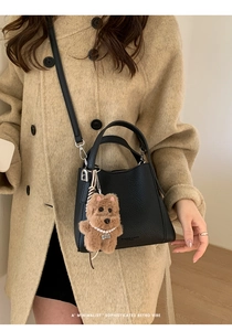 Detail of black pebbled leather bucket bag with cute plush puppy charm and logo print