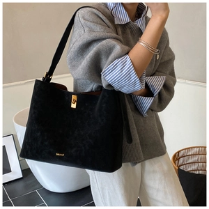 Detail of a black suede tote bag with golden twist lock and brand logo on shoulder
