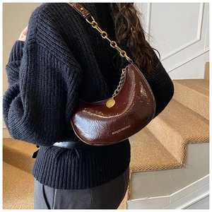 Detail of dark brown dumpling bag with glossy wrinkled leather and golden chain