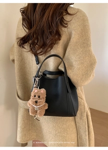 Close-up of black lychee leather bucket bag with cute brown plush bear charm